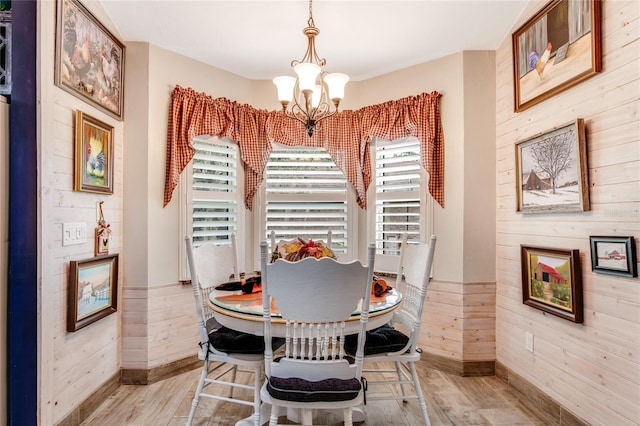 dining room featuring wood walls, light wood-type flooring, and an inviting chandelier