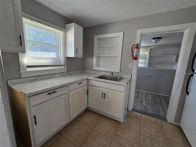 kitchen featuring built in shelves, light tile patterned floors, white cabinetry, and sink