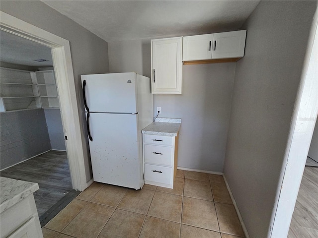 kitchen featuring white refrigerator, light tile patterned flooring, and white cabinetry