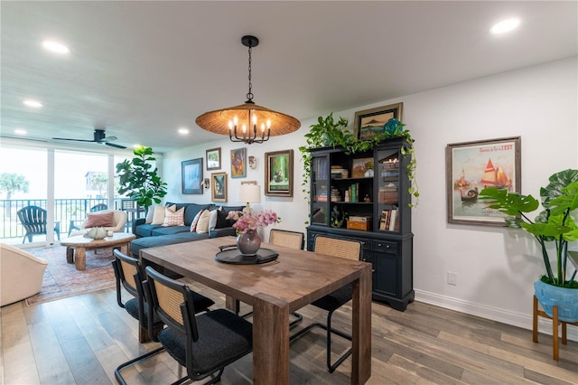 dining room featuring ceiling fan with notable chandelier, expansive windows, and wood-type flooring