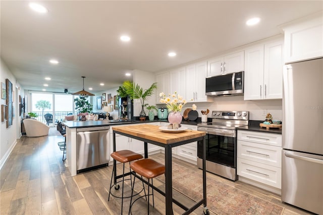 kitchen featuring kitchen peninsula, pendant lighting, a breakfast bar area, white cabinets, and appliances with stainless steel finishes