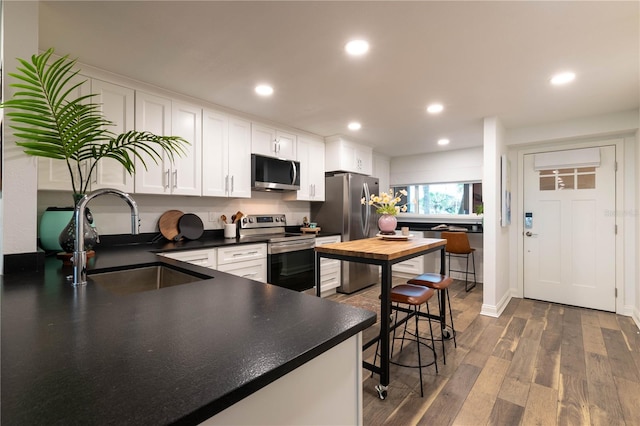 kitchen with white cabinetry, sink, dark hardwood / wood-style flooring, kitchen peninsula, and appliances with stainless steel finishes