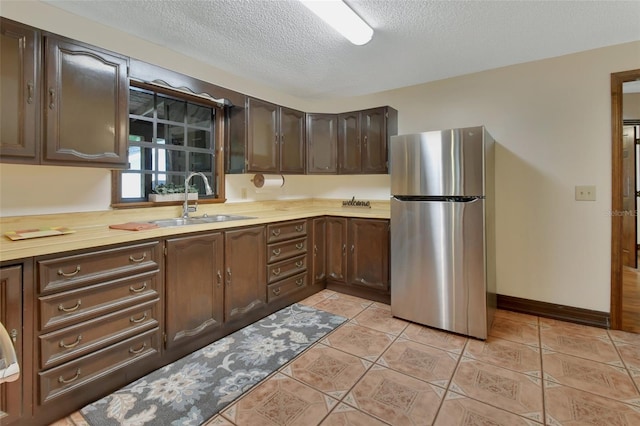 kitchen featuring sink, stainless steel fridge, a textured ceiling, light tile patterned flooring, and dark brown cabinetry