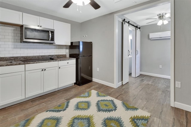 kitchen featuring a wall unit AC, a barn door, white cabinets, and black appliances