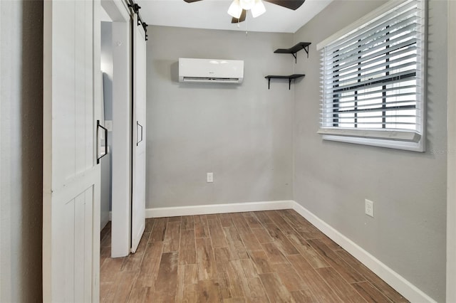 interior space featuring a barn door, light hardwood / wood-style flooring, an AC wall unit, and ceiling fan