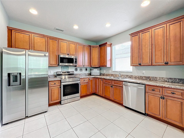 kitchen featuring sink, light tile patterned floors, a textured ceiling, light stone counters, and stainless steel appliances