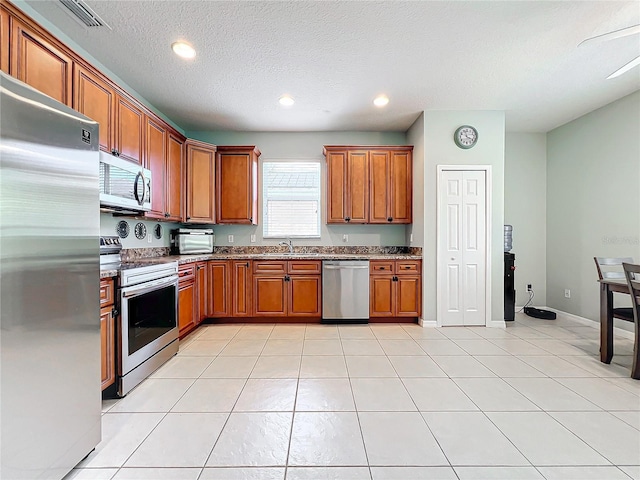 kitchen featuring sink, light tile patterned floors, stainless steel appliances, and a textured ceiling