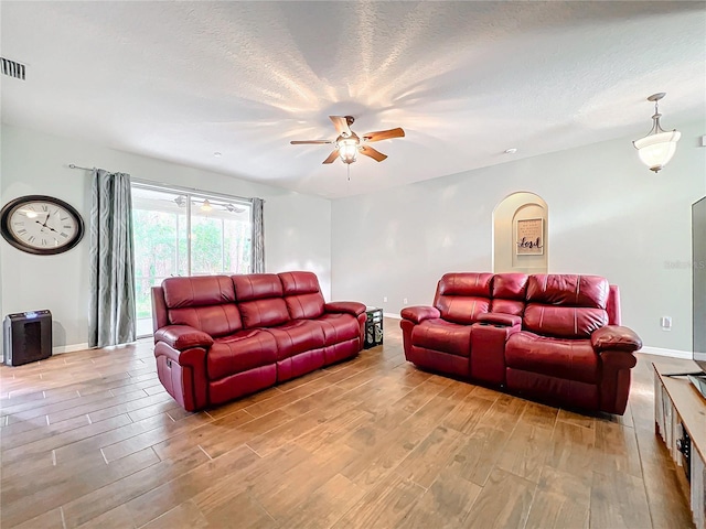 living room with a textured ceiling, light wood-type flooring, and ceiling fan