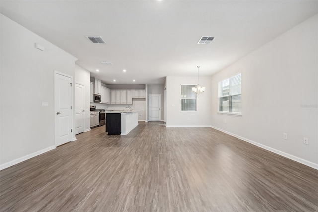 unfurnished living room featuring hardwood / wood-style floors, sink, and an inviting chandelier