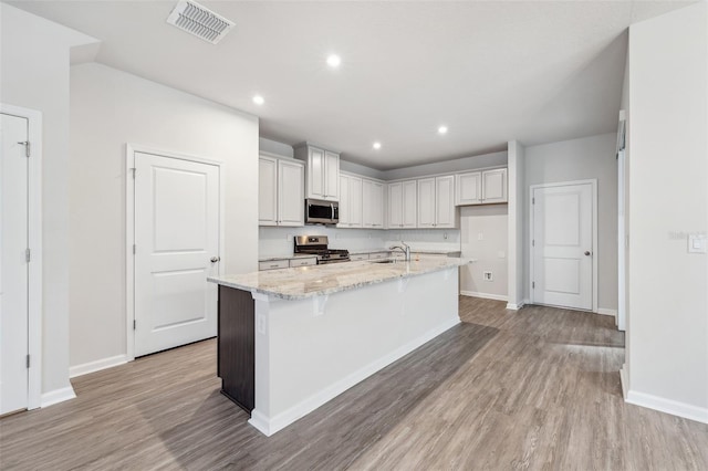 kitchen featuring a kitchen island with sink, sink, light hardwood / wood-style floors, light stone counters, and stainless steel appliances