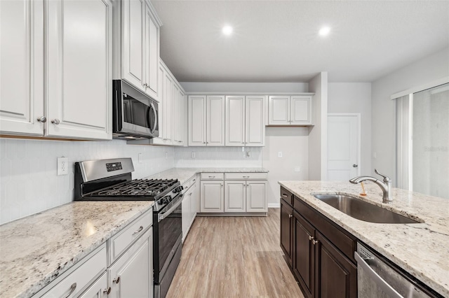 kitchen featuring white cabinetry, sink, stainless steel appliances, and light stone counters