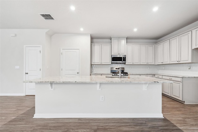 kitchen featuring a kitchen bar, appliances with stainless steel finishes, light stone counters, and a kitchen island with sink