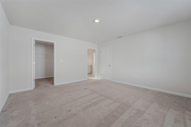 unfurnished bedroom with light carpet, a walk in closet, and a closet