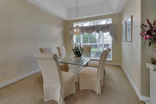 dining space with a raised ceiling, light carpet, and a notable chandelier