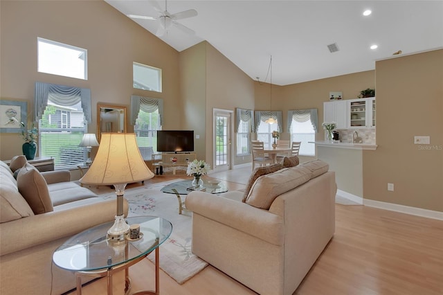 living room with ceiling fan, light hardwood / wood-style flooring, and a high ceiling