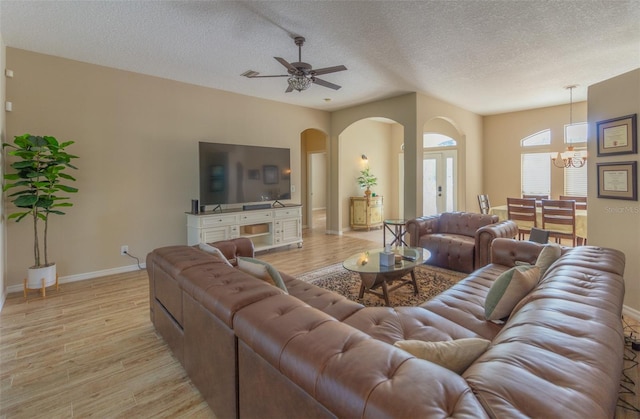 living room with ceiling fan with notable chandelier, a textured ceiling, and light hardwood / wood-style flooring