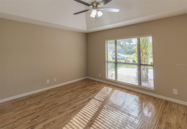 empty room with wood-type flooring, a textured ceiling, a tray ceiling, and ceiling fan