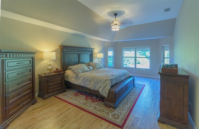 bedroom with light wood-type flooring, a raised ceiling, and ceiling fan