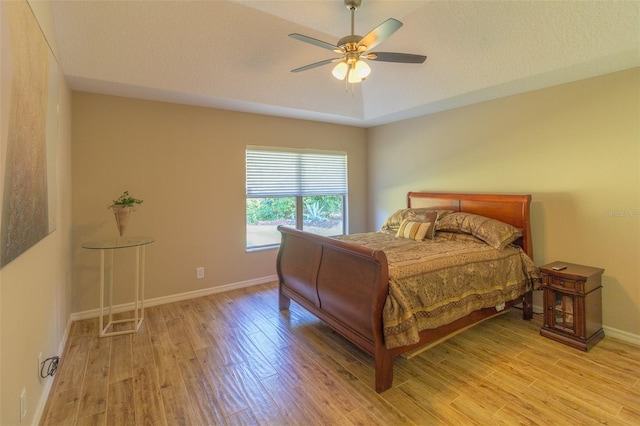 bedroom featuring a tray ceiling, ceiling fan, light hardwood / wood-style flooring, and a textured ceiling