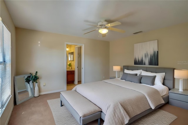 bedroom featuring ceiling fan, light colored carpet, and ensuite bath