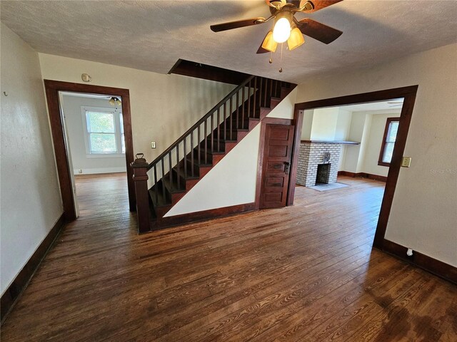 unfurnished living room featuring ceiling fan, a fireplace, dark wood-type flooring, and a textured ceiling