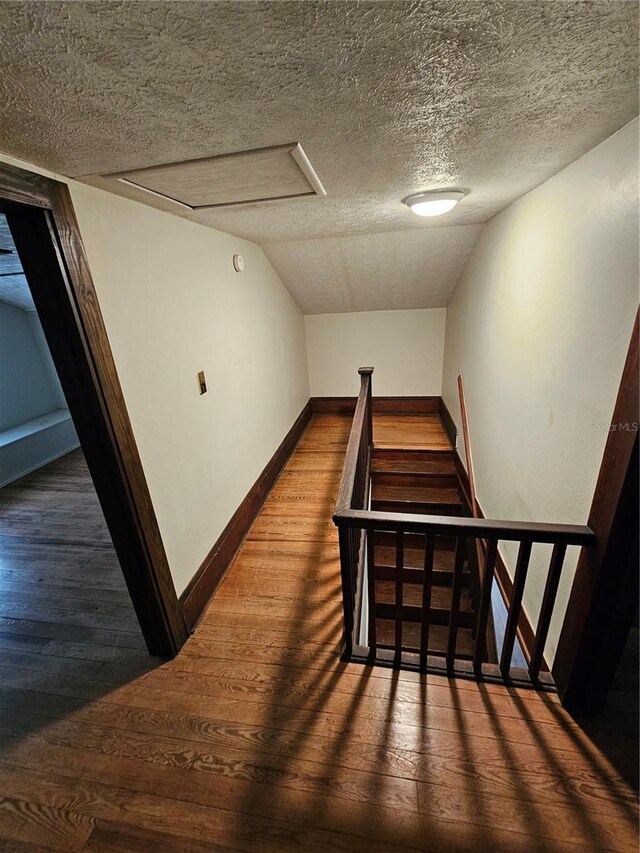 stairs with hardwood / wood-style floors, lofted ceiling, and a textured ceiling