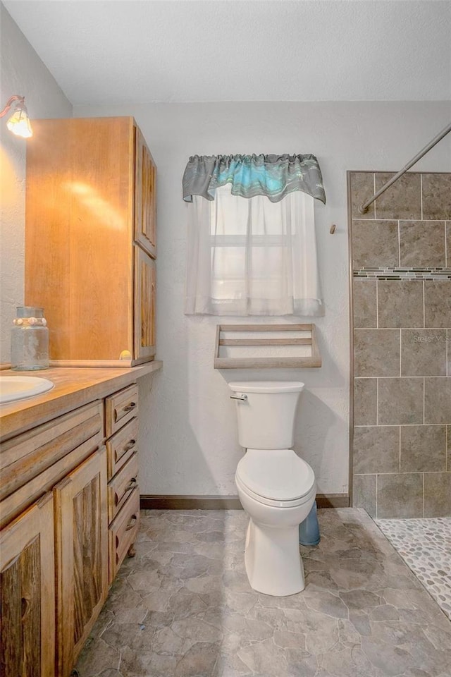 bathroom with a tile shower, vanity, and toilet