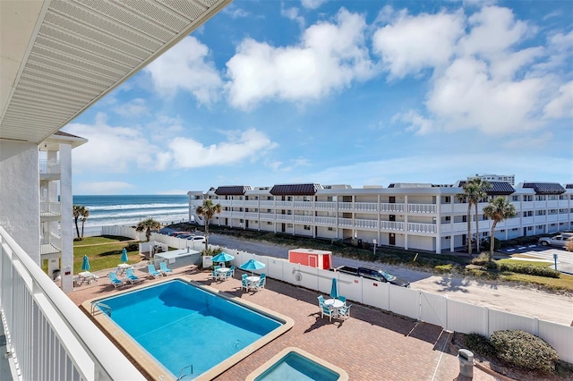 view of pool with a patio area, a water view, and a view of the beach