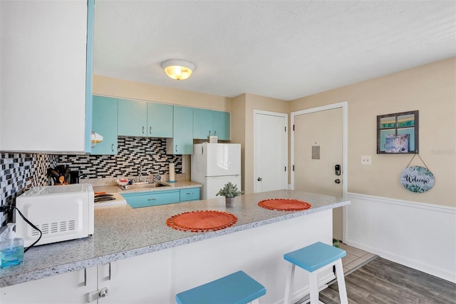 kitchen with a kitchen breakfast bar, dark hardwood / wood-style flooring, backsplash, kitchen peninsula, and white appliances