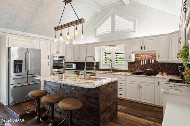 kitchen featuring beam ceiling, stainless steel appliances, light stone counters, high vaulted ceiling, and a center island with sink