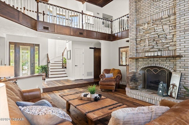 living room featuring a barn door, wood-type flooring, a towering ceiling, and a brick fireplace