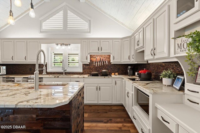 kitchen featuring pendant lighting, white cabinets, vaulted ceiling, light stone countertops, and dark hardwood / wood-style flooring