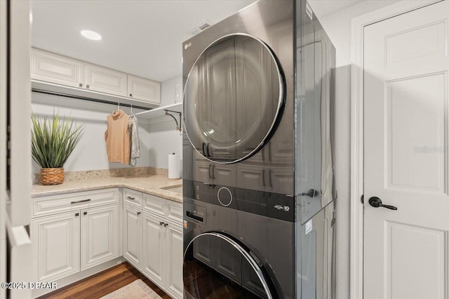 washroom with stacked washer / dryer, dark wood-type flooring, and cabinets