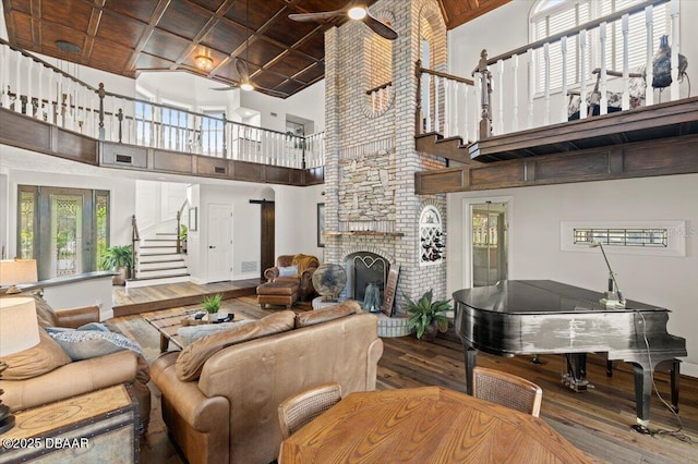 living room featuring ceiling fan, hardwood / wood-style floors, a towering ceiling, a fireplace, and wood ceiling