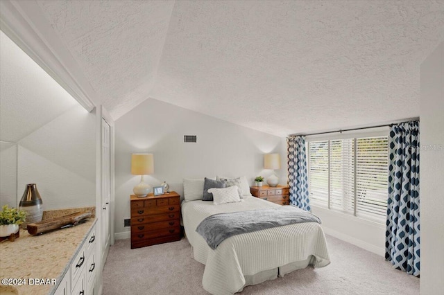 bedroom with a textured ceiling, light carpet, and lofted ceiling