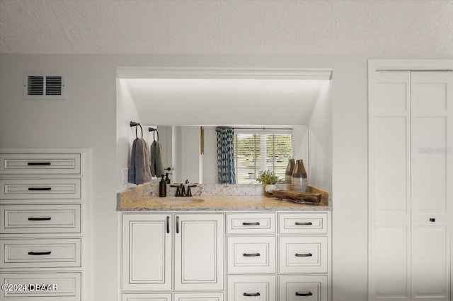 bar featuring a textured ceiling, light stone counters, white cabinetry, and sink