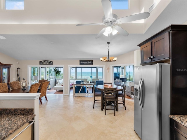 kitchen with ceiling fan with notable chandelier, hanging light fixtures, stainless steel fridge, dark stone countertops, and dark brown cabinetry