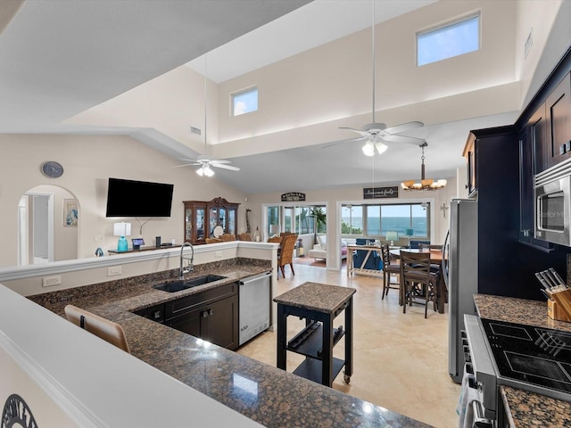 kitchen with a towering ceiling, ceiling fan with notable chandelier, stainless steel appliances, sink, and decorative light fixtures