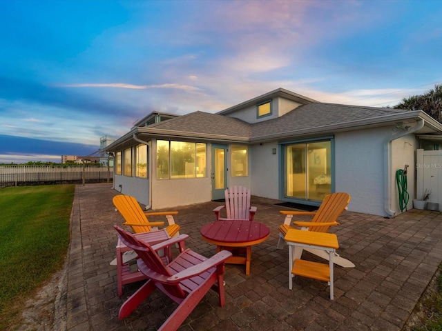 back house at dusk with a yard, a patio, and a sunroom