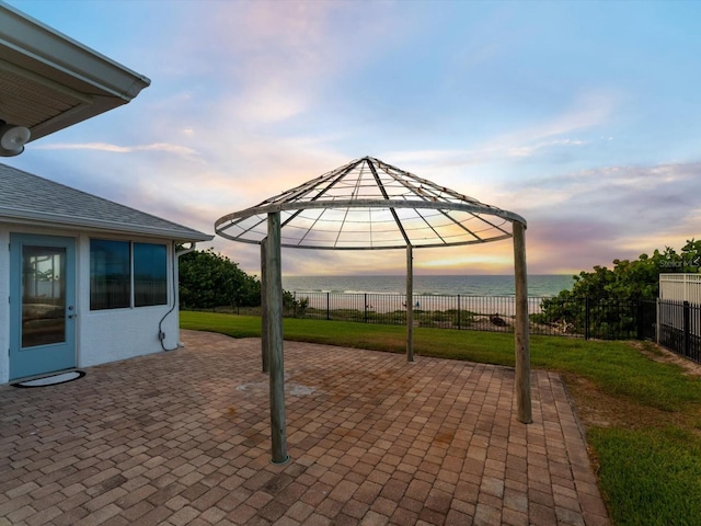 patio terrace at dusk with a gazebo, a water view, and a lawn