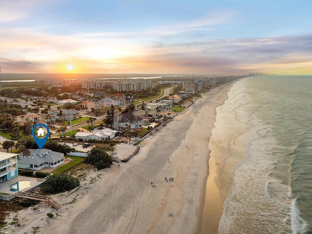 aerial view at dusk featuring a view of the beach and a water view