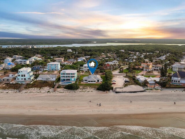 aerial view at dusk featuring a water view and a view of the beach