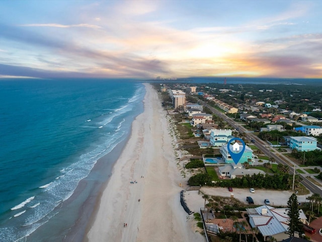 aerial view at dusk with a water view and a beach view