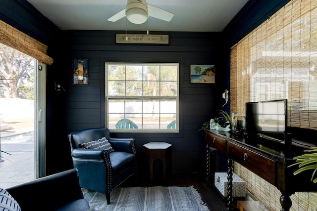 sitting room with ceiling fan and wood walls