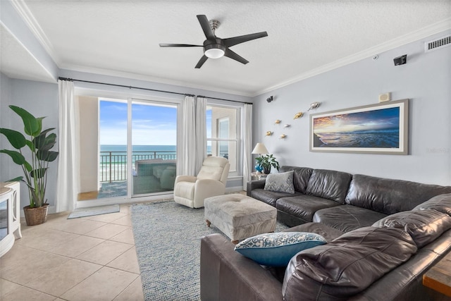 tiled living room with ceiling fan, a water view, ornamental molding, and a textured ceiling