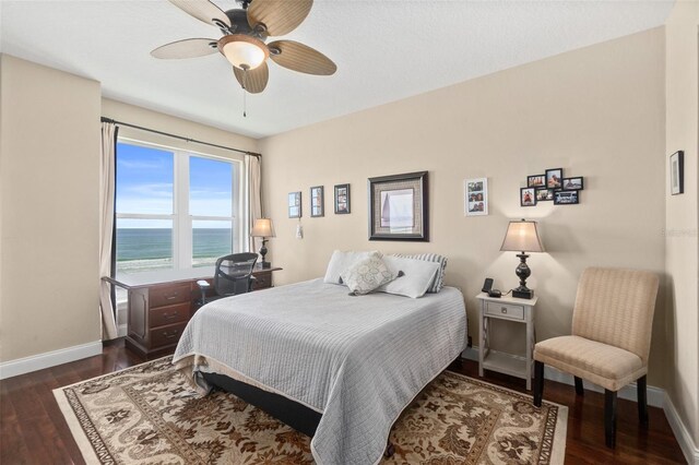 bedroom with ceiling fan, dark hardwood / wood-style floors, and a water view