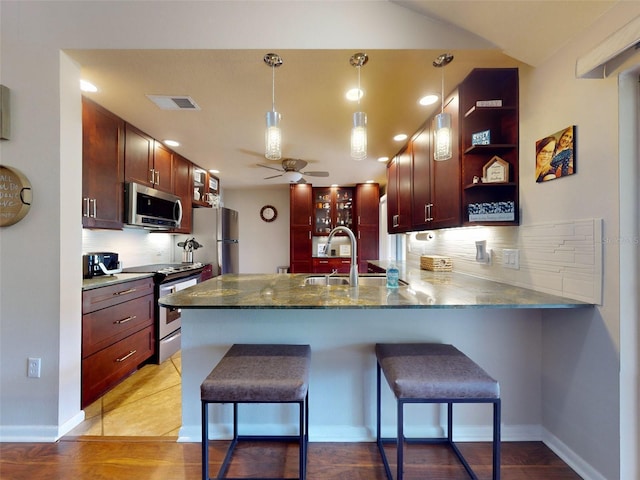 kitchen with kitchen peninsula, a breakfast bar, decorative light fixtures, sink, and appliances with stainless steel finishes