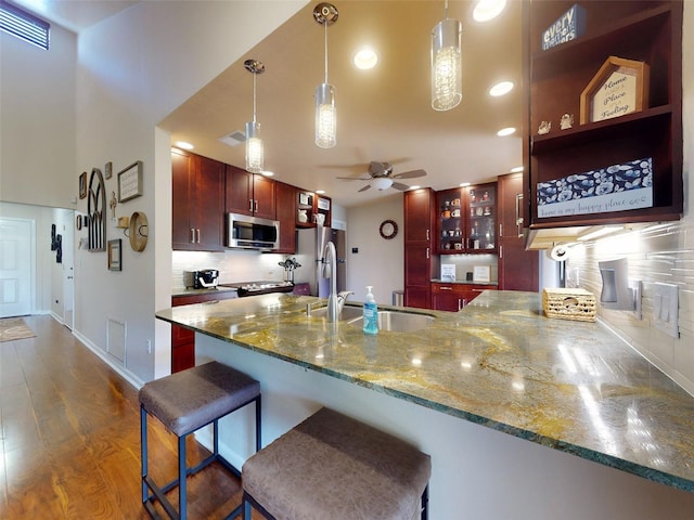 kitchen featuring pendant lighting, stainless steel appliances, kitchen peninsula, light stone countertops, and a breakfast bar area