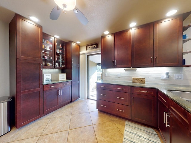 kitchen featuring backsplash, dark stone countertops, light tile patterned flooring, and ceiling fan