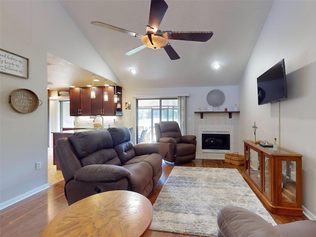 living room featuring light wood-type flooring, a tiled fireplace, high vaulted ceiling, and ceiling fan